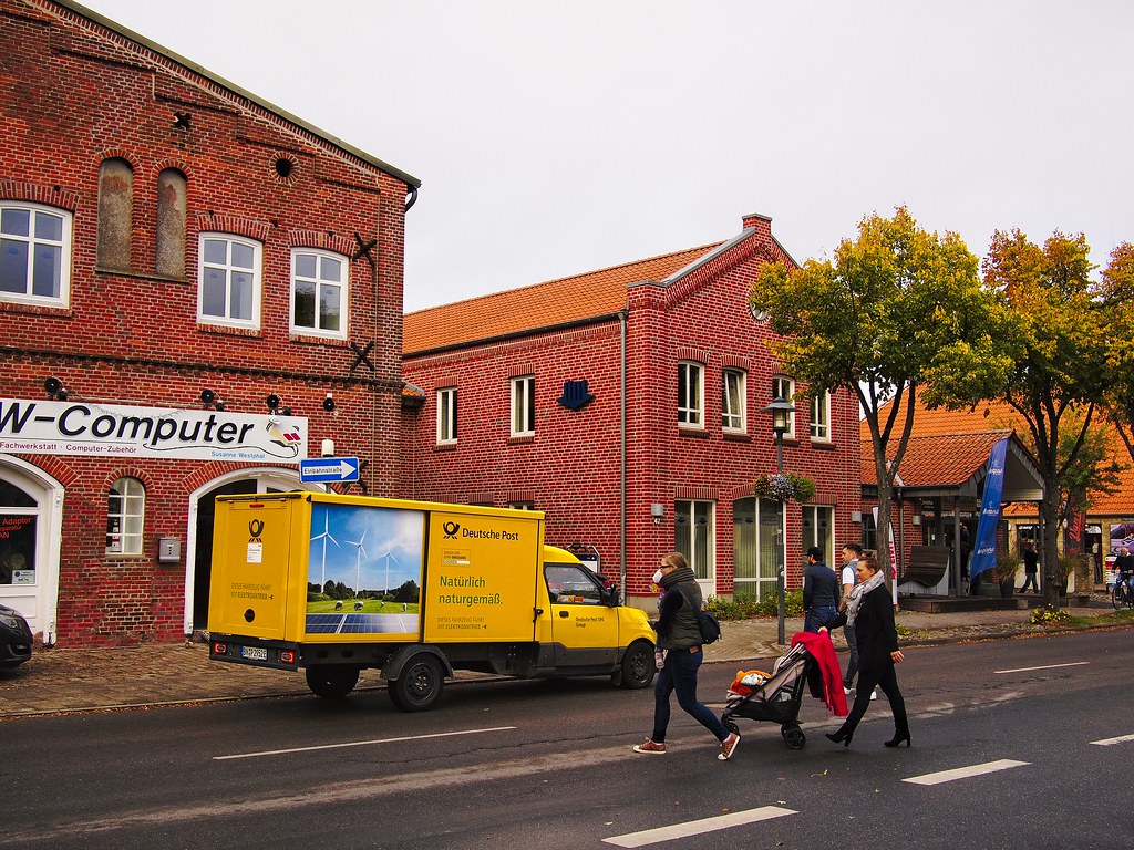 an electric delivery van drops off parcels on a street. a group of people are crossing the road next to it