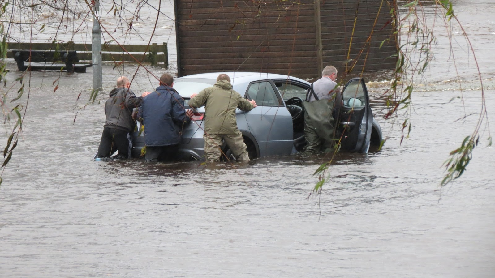 several men pushing a car through flood water