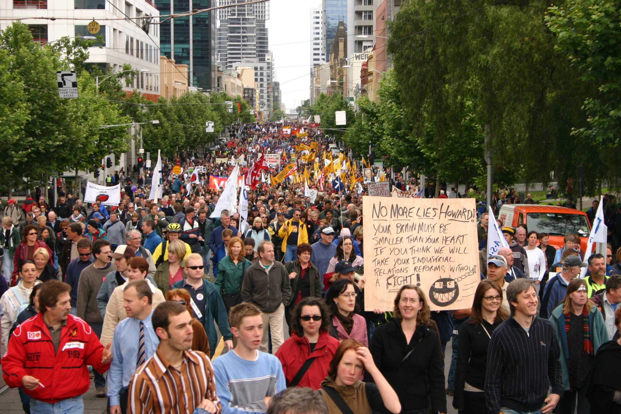 a protest filling a tree-lined street in a major urban area. the cause of the protest is unclear
