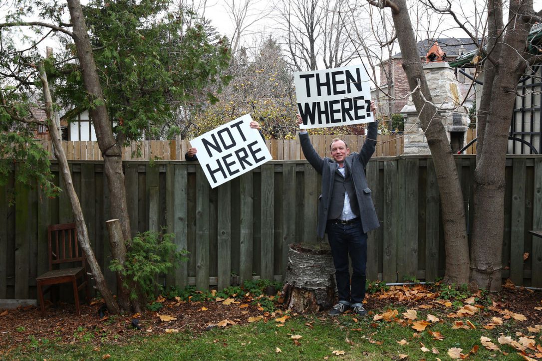 one person holds up a sign saying 'not here.' a man standing next to them holds up a sign saying 'then where?'