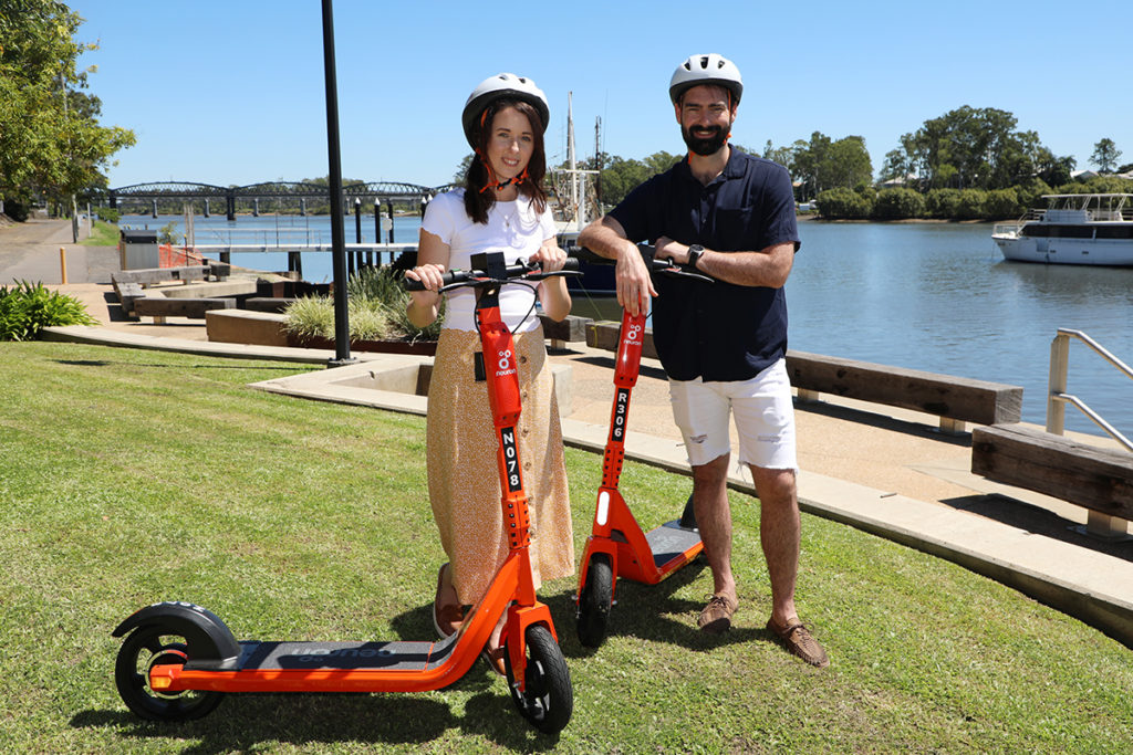 two people standing next to e-scooters