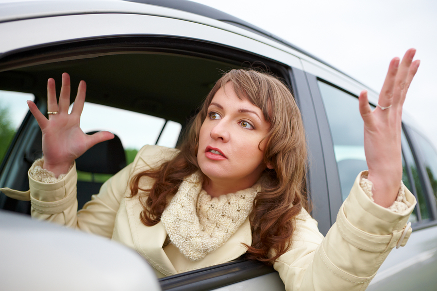 a young woman leaning out of a window of a car, arms in the air, clearly frustrated